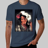 Un t-shirt unisexe, disponible en plusieurs couleurs. Sur la poitrine, une grande image rectangulaire en couleurs représente une personne souriant face à l’objectif. Cette personne porte un maquillage vif, un accessoire fleuri dans les cheveux et une tenue à motifs. L’arrière-plan est sombre, ce qui met en valeur le visage lumineux. Le portrait est encadré dans un rectangle noir. Le nom « Marsha P. Johnson » apparaît imprimé sous l’image selon le modèle du t-shirt présenté.