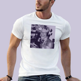 Portrait carré imprimé sur un t-shirt. L’image montre une personne souriante dans un environnement intérieur, tenant un verre à la main. Elle porte une coiffure ornée de nombreuses fleurs et des bijoux visibles autour du cou. L’ambiance évoque une scène festive. Le portrait est présenté dans une teinte violette sur fond clair.