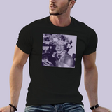 Portrait carré imprimé sur un t-shirt. L’image montre une personne souriante dans un environnement intérieur, tenant un verre à la main. Elle porte une coiffure ornée de nombreuses fleurs et des bijoux visibles autour du cou. L’ambiance évoque une scène festive. Le portrait est présenté dans une teinte violette sur fond clair.