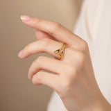 Main féminine portant une bague dorée en forme de ciseaux, mise en avant sur un fond doux et neutre.