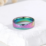 Bague facettée en carbure de tungstène poli vue de face. Les facettes extérieures présentent des reflets multicolores irisés. L’intérieur lisse contraste avec la surface extérieure sculptée.