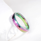 Bague en carbure de tungstène poli posée sur un support clair. La surface facettée reflète des nuances prismatiques métalliques. La forme circulaire et l’épaisseur de l’anneau sont visibles.