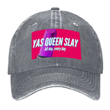 Casquette de style baseball avec visière incurvée. Tissu à effet délavé, visible en trois déclinaisons : gris foncé, gris clair et beige. Sur l’avant, un large rectangle rose vif imprimé. Au centre, texte blanc « YAS QUEEN SLAY » et en plus petit « All day, every day ». À gauche du texte, partie d’un rouge à lèvres violet en gros plan. L’impression est rectangulaire et occupe la zone frontale de la casquette.
