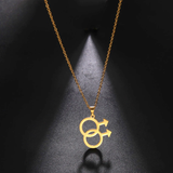 Collier composé d’une fine chaîne métallique portant un pendentif formé de deux cercles entrelacés, chacun prolongé d’une flèche orientée vers l’extérieur. Le pendentif représente le symbole masculin doublé. L’ensemble existe en finition dorée ou argentée. Le pendentif forme une silhouette nette, géométrique, avec des lignes lisses et une surface uniforme. La lumière glisse sur le métal et crée une ombre ovale sous le pendentif, soulignant la forme des deux cercles reliés.