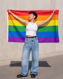 Grand drapeau Pride arc-en-ciel tenu ouvert par une femme en extérieur
