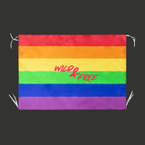Drapeau rectangulaire avec bandes horizontales rouge, orange, jaune, vert, bleu et violet formant le drapeau arc-en-ciel Pride. Au centre apparaît le texte rose vif "Wild &amp; Free" dans une typographie manuscrite dynamique. Des bandes de fixation blanches sont visibles aux coins.