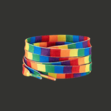 Paire de lacets plats enroulés. Les lacets présentent des bandes multicolores horizontales correspondant aux couleurs du drapeau Pride. Ce modèle a des motifs carré. Les couleurs sont vives et contrastées. Les extrémités sont rigides. Présentation sur fond gris, sans texte intégré.