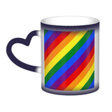 Mug en céramique avec poignée en forme de cœur. À froid, l’extérieur est uniformément coloré (noir, bleu ou rouge) avec de petits points blancs. Au contact de la chaleur, le centre devient blanc et révèle un grand rectangle composé de bandes diagonales arc-en-ciel : rouge, orange, jaune, vert, bleu et violet, orientées du coin supérieur gauche vers le coin inférieur droit. Le contraste reste visible entre la zone éclaircie et la couleur d’origine du mug.