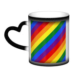Mug en céramique avec poignée en forme de cœur. À froid, l’extérieur est uniformément coloré (noir, bleu ou rouge) avec de petits points blancs. Au contact de la chaleur, le centre devient blanc et révèle un grand rectangle composé de bandes diagonales arc-en-ciel : rouge, orange, jaune, vert, bleu et violet, orientées du coin supérieur gauche vers le coin inférieur droit. Le contraste reste visible entre la zone éclaircie et la couleur d’origine du mug.
