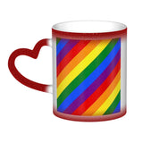 Mug en céramique avec poignée en forme de cœur. À froid, l’extérieur est uniformément coloré (noir, bleu ou rouge) avec de petits points blancs. Au contact de la chaleur, le centre devient blanc et révèle un grand rectangle composé de bandes diagonales arc-en-ciel : rouge, orange, jaune, vert, bleu et violet, orientées du coin supérieur gauche vers le coin inférieur droit. Le contraste reste visible entre la zone éclaircie et la couleur d’origine du mug.