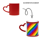 Mug en céramique avec poignée en forme de cœur. À froid, l’extérieur est uniformément coloré (noir, bleu ou rouge) avec de petits points blancs. Au contact de la chaleur, le centre devient blanc et révèle un grand rectangle composé de bandes diagonales arc-en-ciel : rouge, orange, jaune, vert, bleu et violet, orientées du coin supérieur gauche vers le coin inférieur droit. Le contraste reste visible entre la zone éclaircie et la couleur d’origine du mug.