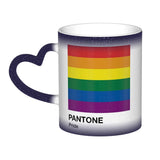 Mug en céramique avec poignée en forme de cœur. À froid, la surface extérieure est uniformément colorée (noir, bleu ou rouge) avec de petits points blancs dispersés. Au contact de la chaleur, le centre du mug devient blanc et révèle un carré composé de six bandes horizontales : rouge en haut, puis orange, jaune, vert, bleu et violet. Sous le carré figurent les mots « PANTONE » puis « Pride ». Le contraste entre la zone blanche révélée et la couleur d’origine reste visible autour du mug.