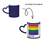 Mug en céramique avec poignée en forme de cœur. À froid, la surface extérieure est uniformément colorée (noir, bleu ou rouge) avec de petits points blancs dispersés. Au contact de la chaleur, le centre du mug devient blanc et révèle un carré composé de six bandes horizontales : rouge en haut, puis orange, jaune, vert, bleu et violet. Sous le carré figurent les mots « PANTONE » puis « Pride ». Le contraste entre la zone blanche révélée et la couleur d’origine reste visible autour du mug.