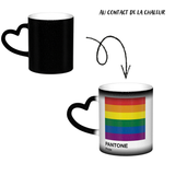 Mug en céramique avec poignée en forme de cœur. À froid, la surface extérieure est uniformément colorée (noir, bleu ou rouge) avec de petits points blancs dispersés. Au contact de la chaleur, le centre du mug devient blanc et révèle un carré composé de six bandes horizontales : rouge en haut, puis orange, jaune, vert, bleu et violet. Sous le carré figurent les mots « PANTONE » puis « Pride ». Le contraste entre la zone blanche révélée et la couleur d’origine reste visible autour du mug.