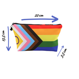 Trousse rectangulaire de petite taille, imprimée du motif “Pride Progress”. Le motif combine des bandes horizontales rouge, orange, jaune, vert, bleu, violet, et à gauche une chevron verticale avec rose, bleu clair, blanc, marron, noir. La trousse est ouverte — la doublure intérieure est d’un tissu sombre uni. Une fermeture éclair traverse la largeur supérieure. La trousse apparaît vide ou très légèrement ouverte, montrant l’intérieur sombre, sans objets à l’intérieur visibles.