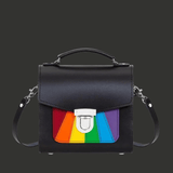 Sac rigide en cuir noir de format compact, avec poignée supérieure et bandoulière amovible. Sur la face avant, un empiècement cousu en bandes arc-en-ciel Pride. Fermeture métallique push lock centrée. Forme structurée.