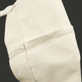 Gros plan sur le tissu du tote bag montrant la texture de la toile écrue et une couture latérale visible.