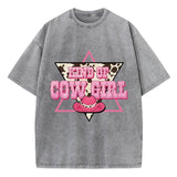T-shirt oversize aux couleurs délavées avec imprimé “Kind of Cowgirl”, triangle rose, motif peau de vache et chapeau cowgirl rose, style western queer.