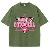 T-shirt oversize aux couleurs délavées avec imprimé “Kind of Cowgirl”, triangle rose, motif peau de vache et chapeau cowgirl rose, style western queer.