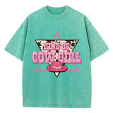T-shirt oversize aux couleurs délavées avec imprimé “Kind of Cowgirl”, triangle rose, motif peau de vache et chapeau cowgirl rose, style western queer.