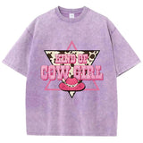 T-shirt oversize aux couleurs délavées avec imprimé “Kind of Cowgirl”, triangle rose, motif peau de vache et chapeau cowgirl rose, style western queer.