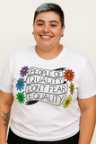 T-shirt unisexe, coupe droite, fond de couleur unie (exemple noir ou blanc selon version). Sur le devant, au centre de la poitrine, un texte en lettres majuscules : « PEOPLE OF QUALITY DON’T FEAR EQUALITY ». Autour du texte, de part et d’autre, des dessins de fleurs stylisées — chaque fleur a des pétales d’une couleur différente (vert, bleu, jaune, rouge, violet, etc.). Les lettres du message sont noires; le fond du t-shirt est uni. L’agencement crée un contraste net entre le texte, les dessins colorés et l