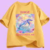  T-shirt unisexe décliné en plusieurs couleurs. Sur le devant, une grande illustration centrale : un dauphin bleu-violet sautant hors de l’eau. Derrière lui, un arc de couleurs et un ciel jaune et violet. Autour, fleurs roses et petits cœurs colorés. Au-dessus : le mot “RAGE” en lettres majuscules rose foncé. En dessous : “CONSUMES ME” dans la même typographie. Le visuel occupe une zone rectangulaire centrée sur le torse. 