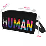 Trousse rectangulaire à fermeture éclair, fond noir. Sur un côté apparaît l’inscription « HUMAN » en caractères majuscules : chaque lettre est remplie de bandes colorées rappelant les couleurs du drapeau de la fierté (ton arc-en-ciel). La trousse a une anse noire sur le côté. Elle peut servir à ranger des objets personnels, des articles de toilette ou des accessoires.