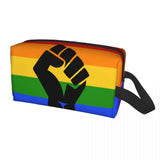 Trousse rectangulaire à fermeture éclair, décorée des six bandes horizontales du drapeau arc-en-ciel : rouge, orange, jaune, vert, bleu et violet. Au centre, un grand poing noir stylisé est imprimé. Une sangle noire est fixée sur le côté droit. Forme allongée destinée à transporter divers objets du quotidien.