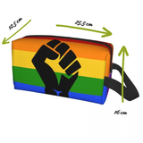 Trousse rectangulaire à fermeture éclair, décorée des six bandes horizontales du drapeau arc-en-ciel : rouge, orange, jaune, vert, bleu et violet. Au centre, un grand poing noir stylisé est imprimé. Une sangle noire est fixée sur le côté droit. Forme allongée destinée à transporter divers objets du quotidien.