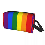 Trousse rectangulaire à fermeture éclair, décorée de six bandes verticales aux couleurs du drapeau arc-en-ciel : violet, bleu, vert, jaune, orange et rouge. Une sangle noire est fixée sur le côté droit. La trousse est de forme allongée et destinée à transporter divers objets du quotidien.