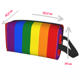Trousse rectangulaire à fermeture éclair, décorée de six bandes verticales aux couleurs du drapeau arc-en-ciel : violet, bleu, vert, jaune, orange et rouge. Une sangle noire est fixée sur le côté droit. La trousse est de forme allongée et destinée à transporter divers objets du quotidien.