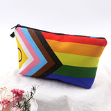 Trousse rectangulaire de petite taille, imprimée du motif “Pride Progress”. Le motif combine des bandes horizontales rouge, orange, jaune, vert, bleu, violet, et à gauche une chevron verticale avec rose, bleu clair, blanc, marron, noir. La trousse est ouverte — la doublure intérieure est d’un tissu sombre uni. Une fermeture éclair traverse la largeur supérieure. La trousse apparaît vide ou très légèrement ouverte, montrant l’intérieur sombre, sans objets à l’intérieur visibles.