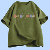 T-shirt à manches courtes présenté à plat. Au centre, le texte « see you in hell » écrit en lettres minuscules, avec un dégradé de couleurs. Autour du texte, de petites étoiles décoratives multicolores. Le motif est centré sur la poitrine. Le t-shirt existe en plusieurs couleurs unies. Aucun autre texte ou image n’est présent.