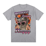 T-shirt à manches courtes. Sur la poitrine, illustration imprimée d’un chat cartoon stylisé — le chat porte des lunettes en forme de cœur de couleur rose, a des ongles longs, et semble entouré d’un motif graphique vif aux teintes chaudes. Au-dessus et en dessous du chat, le texte “YAASSS Queen Slayyy” est visible en lettres colorées. Le design combine humour, couleurs vives et style affirmé.