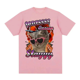 T-shirt à manches courtes. Sur la poitrine, illustration imprimée d’un chat cartoon stylisé — le chat porte des lunettes en forme de cœur de couleur rose, a des ongles longs, et semble entouré d’un motif graphique vif aux teintes chaudes. Au-dessus et en dessous du chat, le texte “YAASSS Queen Slayyy” est visible en lettres colorées. Le design combine humour, couleurs vives et style affirmé.